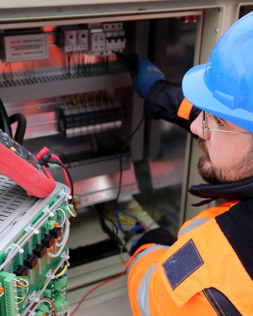 Electrician in high-visibility clothing working on an electrical control panel
