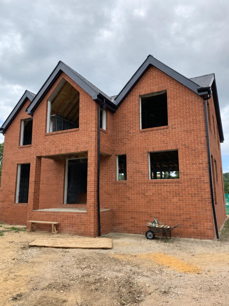 Unfinished red-brick two-storey house with gabled roofs and unglazed window openings