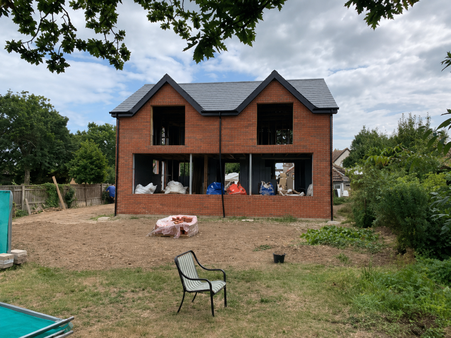 Unfinished red-brick two-storey house with a gabled roof, viewed across the garden
