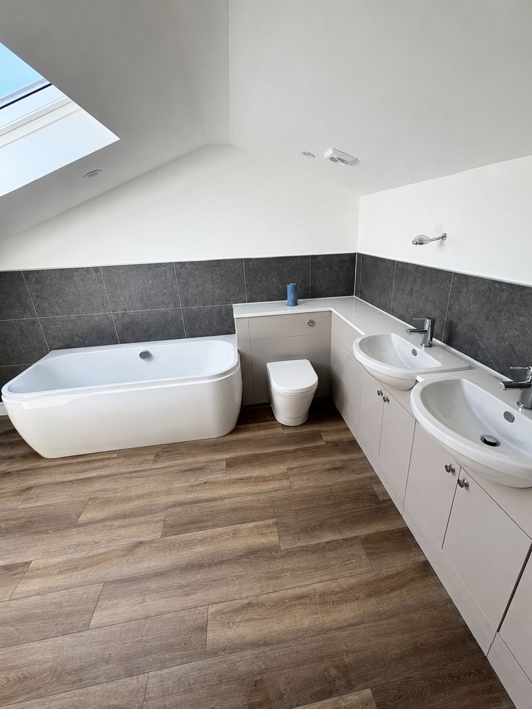Completed bathroom with a bath, toilet, twin basins and wood-effect flooring