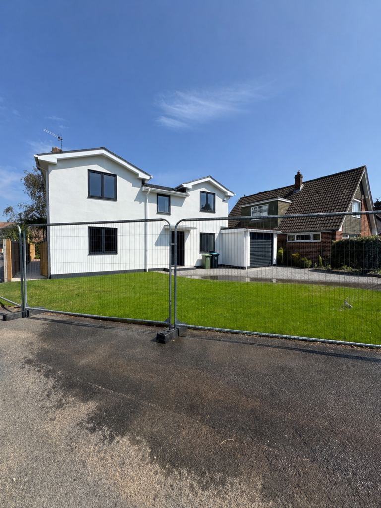 Completed white two-storey extension behind temporary site fencing