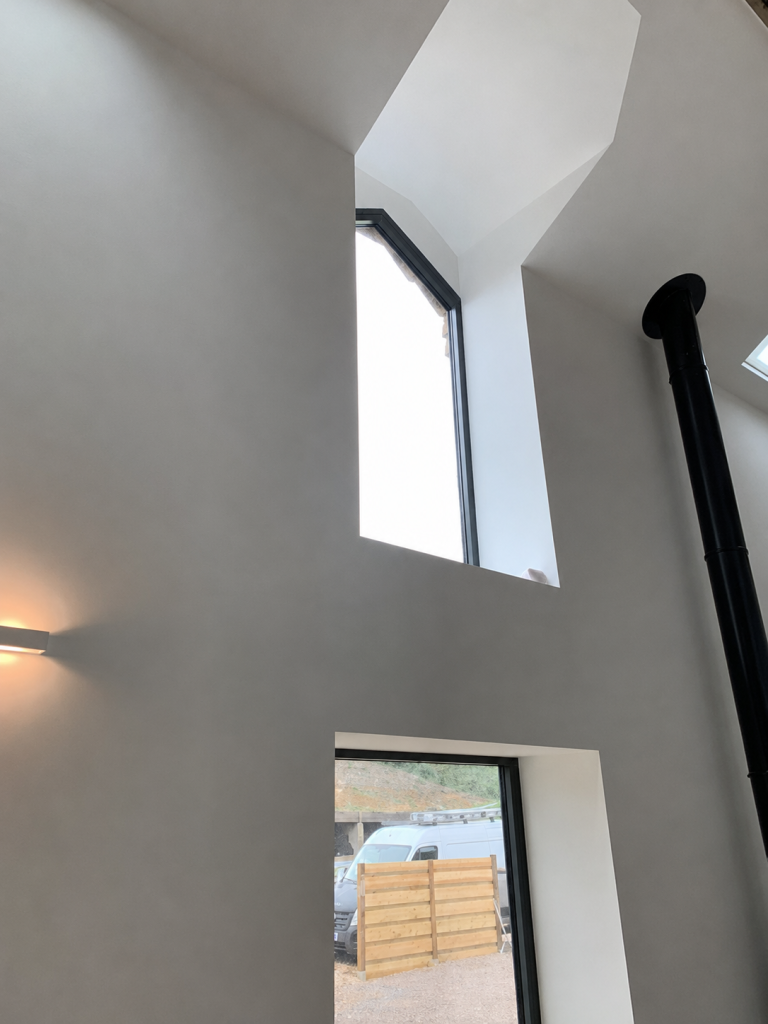 Double-height white interior with high windows and a black stove flue