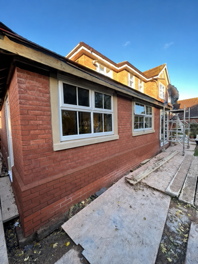 Brick house extension with new white-framed windows and scaffolding